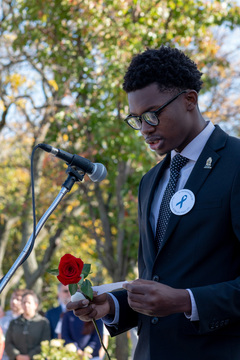 With rose, stone and paper script in hand, Remembrance Scholar Fabryce Fetus reads a statement to the crowd. He places a rose in memory of all of the lives lost on Pan Am flight 103. 