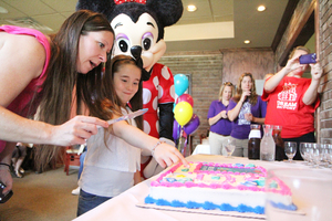 (From left) Kelly Badgley and Emma Louise cut a cake for a surprise put together by Dream Factory Syracuse. Emma asks for a slice from the center, marked with an 